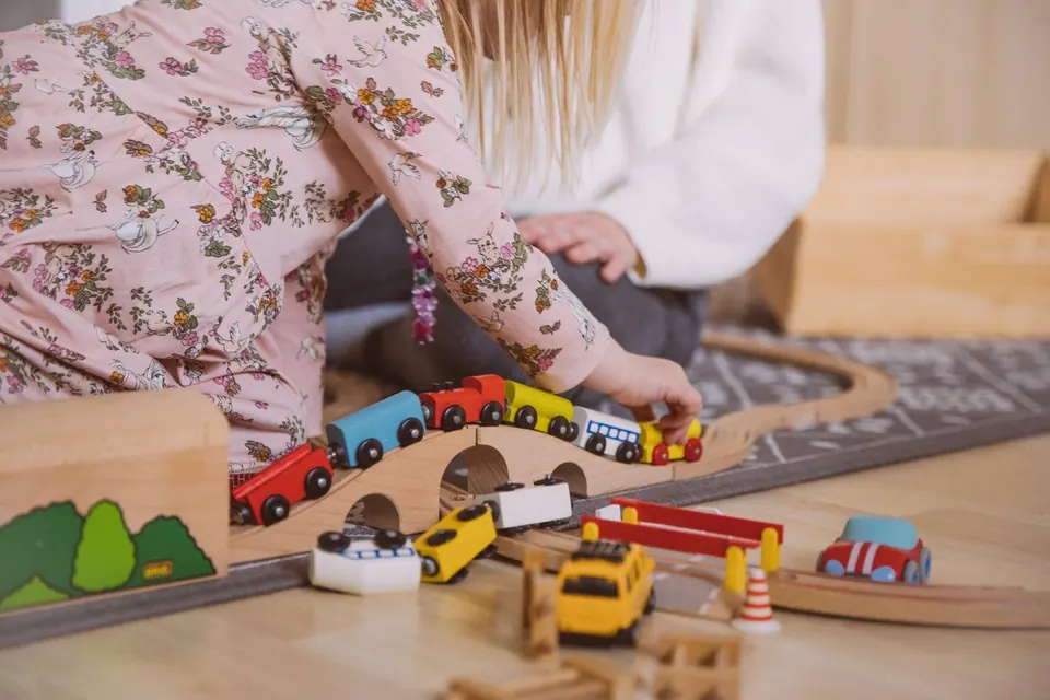 Ein Kind schiebt bunte Holzzüge über eine Brücke der Spielzeugeisenbahn